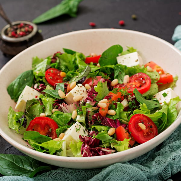 Fresh Italian salad with mixed greens, cherry tomatoes, feta cheese, and pine nuts in a white bowl.