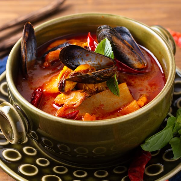 A green bowl of Italian seafood stew with mussels, vegetables, and red chili peppers.