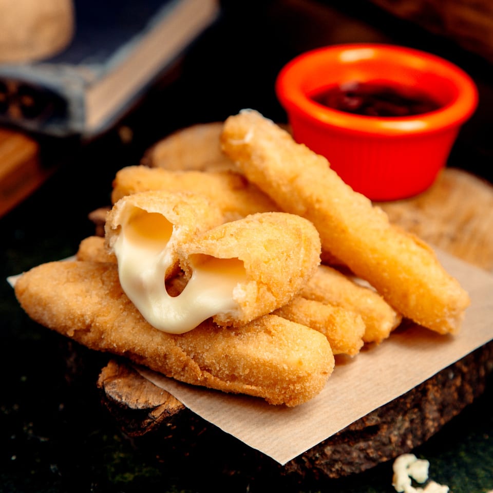 Golden-fried mozzarella sticks with melted cheese oozing out, served with a red dipping sauce.