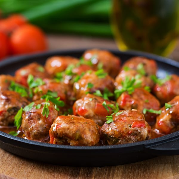 Italian meatballs in a black skillet, garnished with fresh parsley and red sauce.