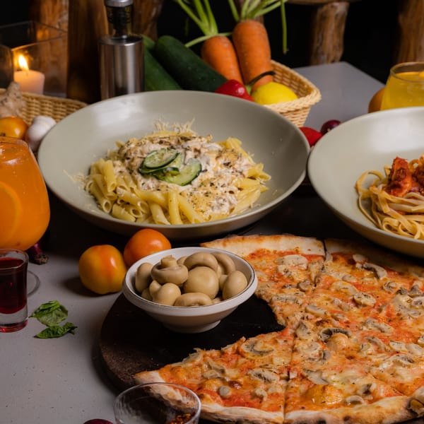 Italian meal with mushroom pizza, creamy pasta, red sauce pasta, and drinks on a table.