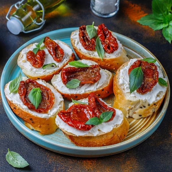 Italian bruschetta with sun-dried tomatoes, creamy cheese, and fresh basil on a blue plate.