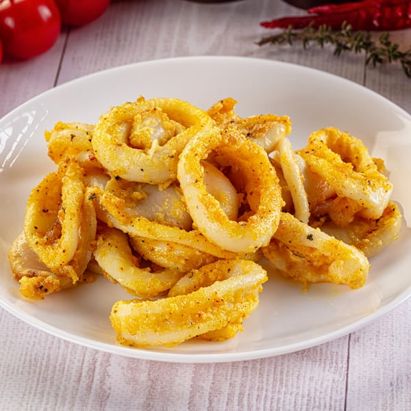 A white plate filled with golden-brown fried calamari rings, seasoned with herbs and spices.