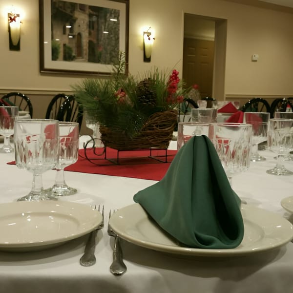 A festive dining table set with white tablecloths, green napkins, and a holiday centerpiece.