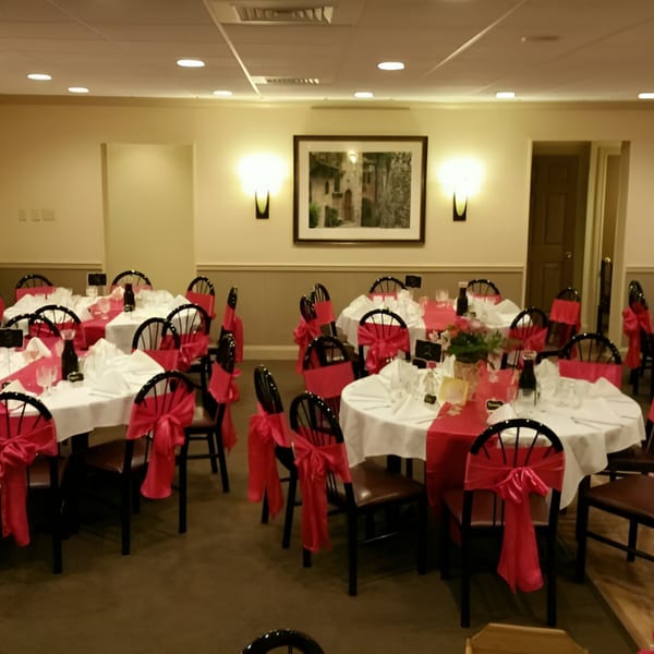 Banquet hall with round tables set with white tablecloths, red runners, and chairs with red sashes.